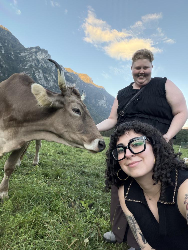 Emilia and a friend posing with a curious cow in front of mountains