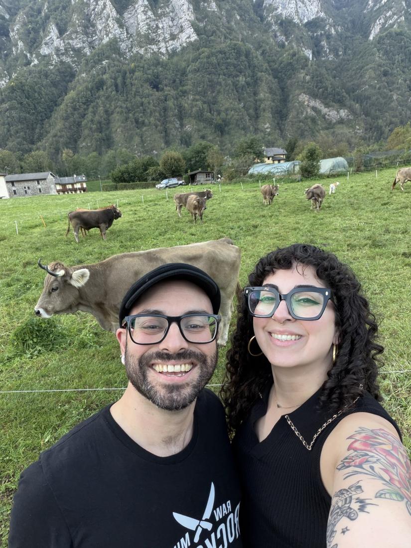 Emilia and Tommy taking a selfie in an alpine pasture with cows behind them