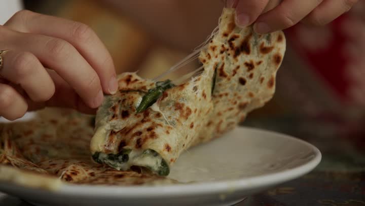 Hands tearing a griddled flatbread filled with melted cheese and greens